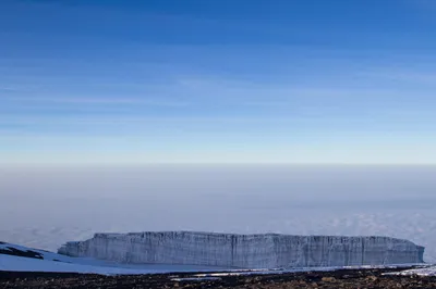 Expansive glacier wall on Mount Kilimanjaro illuminated by soft morning light above the clouds